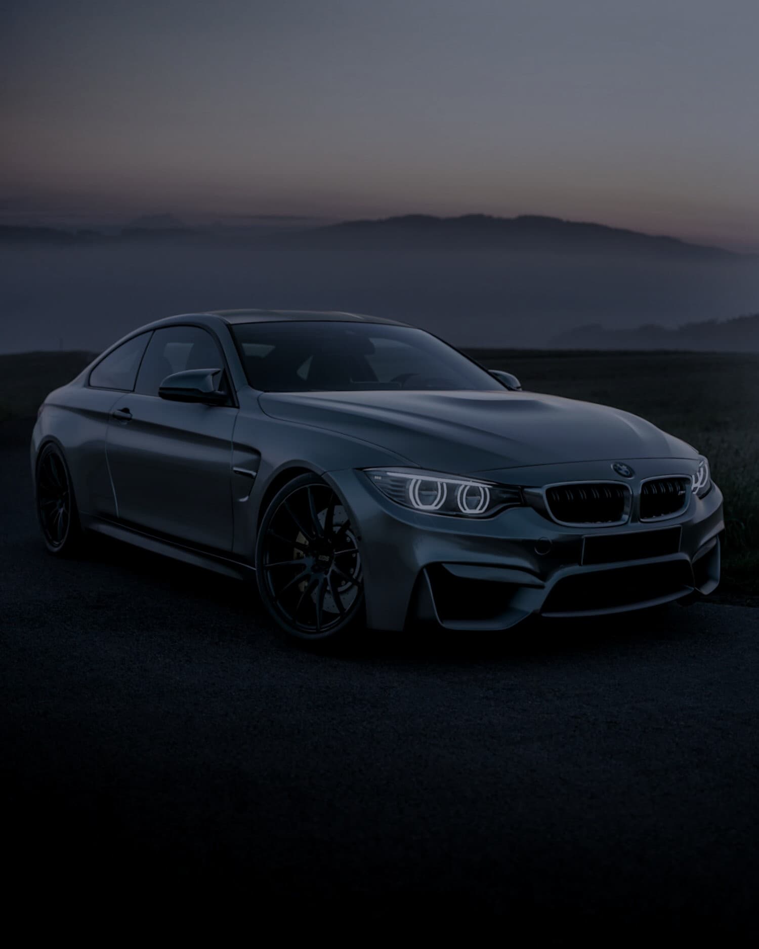 Alacakaranlıkta gri BMW M4, melek göz farları yanık